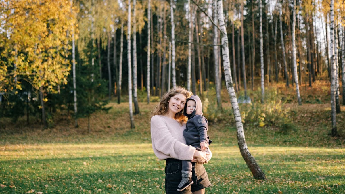 A joyful mother holding her child outdoors in an autumn forest setting.